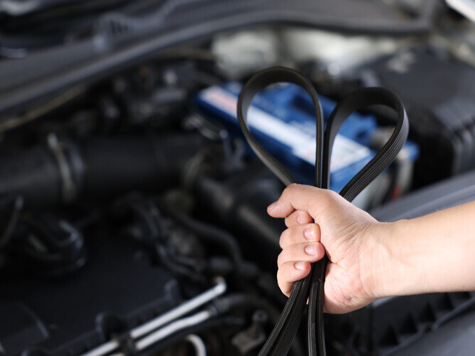 Auto mechanic with timing belt near open hood of car indoors, closeup. Space for text